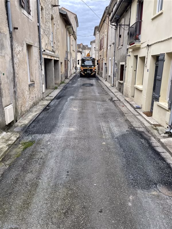 Intervention de maintenance routière par enrobé projeté dans une rue urbaine dégradée