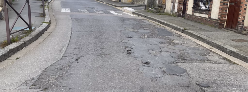 Rue urbaine présentant de nombreuses réparations ponctuelles liées à des cycles de maintenance réactive